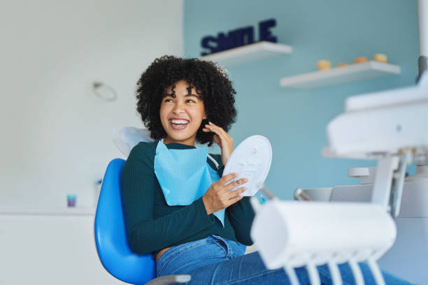 Confident adult woman smiling in a dental chair, mid-30s, bright natural lighting, relaxed setting—capturing a “wow” moment post-veneers