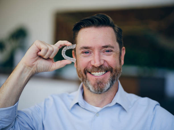 Photo of a middle-aged man holding a clear aligner tray next to his cheek.