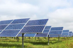 Fileiras de painéis solares azuis montados sobre suportes em um campo com grama verde, indicando uma fazenda de energia solar gerando eletricidade renovável.