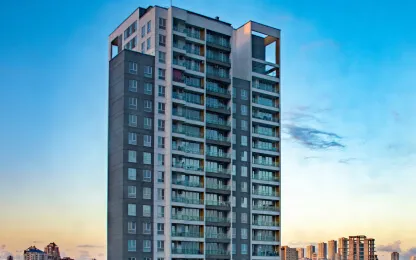 Edifício residencial alto com muitas janelas e varandas, destacando-se contra um céu de fim de tarde com nuvens suaves, sugerindo um ambiente urbano moderno.