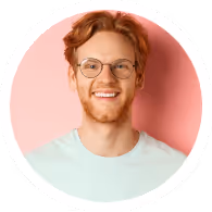 Smiling young man with red hair and glasses wearing a white shirt against a pink background.