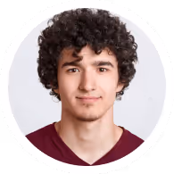 Headshot of a young man with curly dark hair wearing a maroon V-neck shirt, smiling slightly against a light gray background.