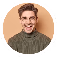 Smiling young man with glasses and brown hair wearing an olive green turtleneck sweater against a beige background.