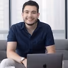 Smiling man sitting on a couch with a laptop in front of him.