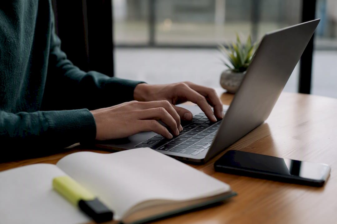 Hands typing near laptop at web developer desk
