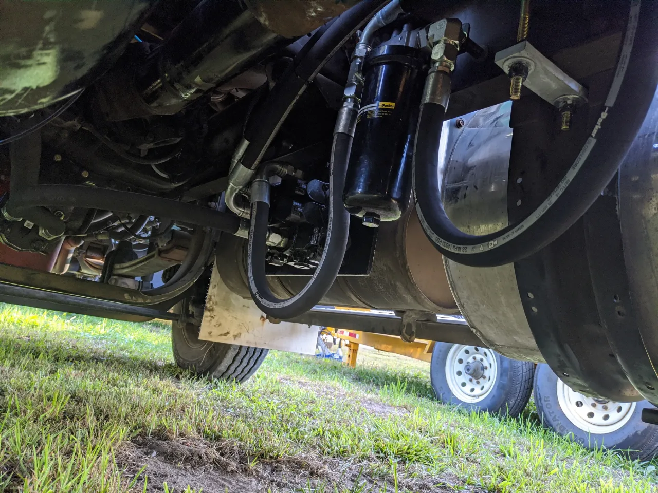 Hydraulic filter assembly mounted under a heavy-duty truck chassis with connected fluid hoses and fittings.