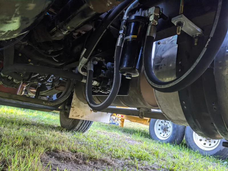 Hydraulic filter assembly mounted under a heavy-duty truck chassis with connected fluid hoses and fittings.