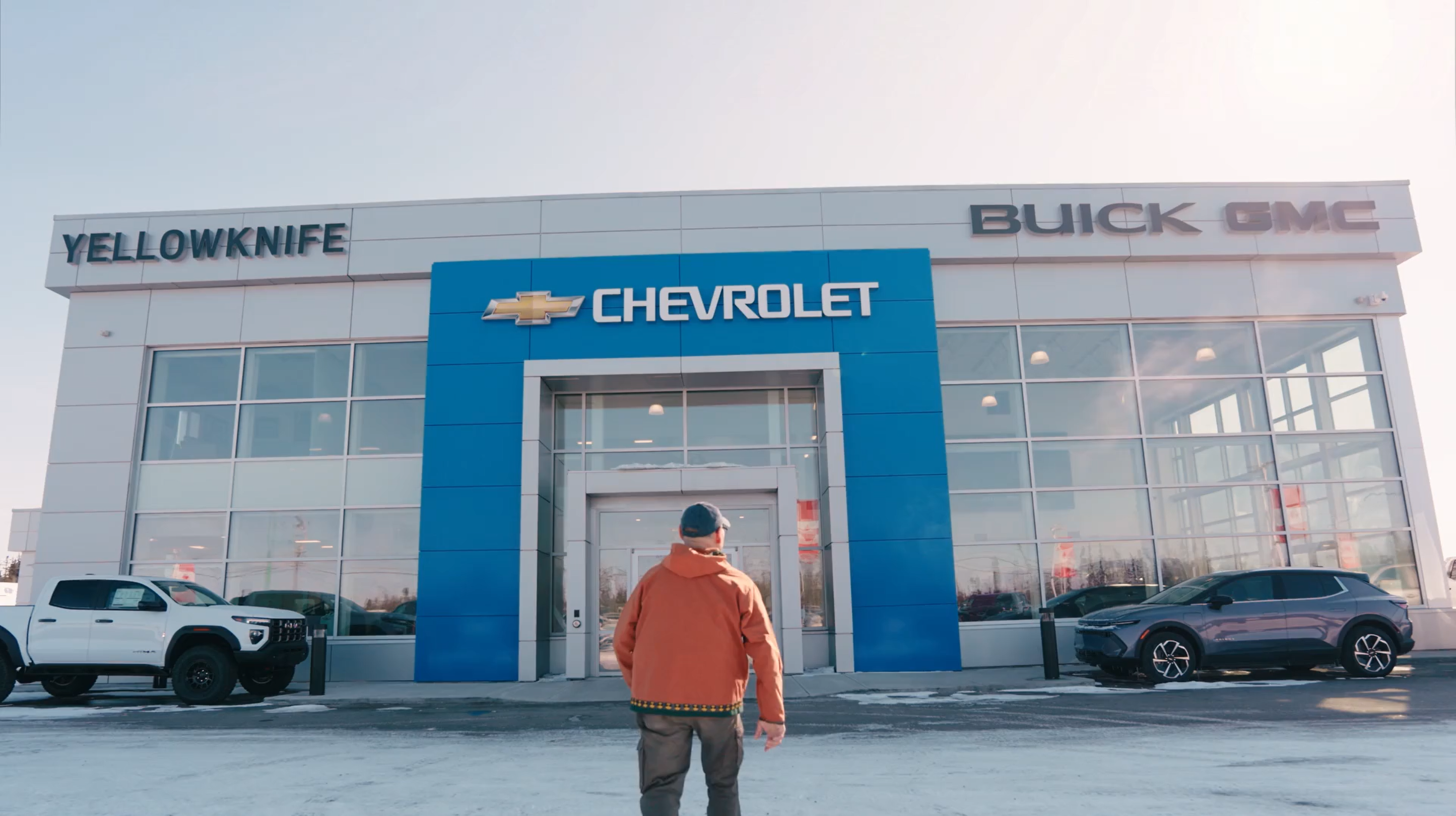 A person stands facing the entrance of a Yellowknife Chevrolet Buick GMC dealership in a snowy environment.