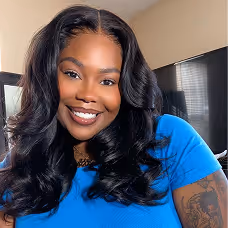 Smiling woman with long wavy black hair wearing a blue shirt in a room with a TV.