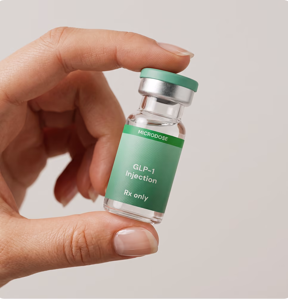 Hand holding a small vial labeled Microdose GLP-1 Injection Rx only against a neutral background.