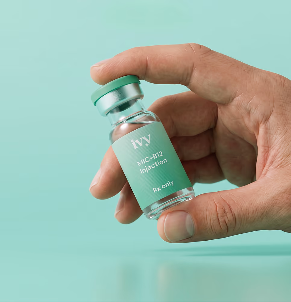 Hand holding a small glass vial labeled 'ivy MIC+B12 Injection Rx only' against a mint green background.