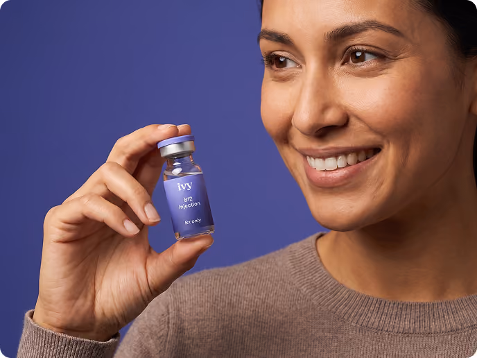 Smiling woman with curly hair holding a small vial labeled 'ivy GLP-1 Injection Rx only' against a teal background.