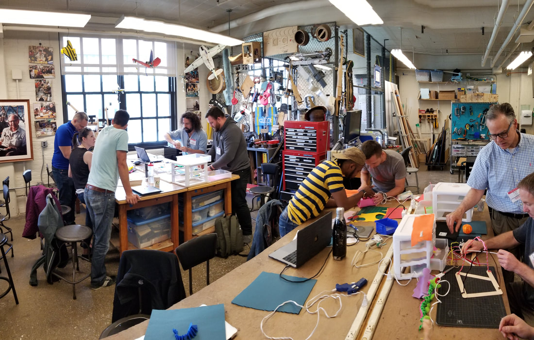 Several people collaborating and working on various projects in a well-equipped makerspace with tools, laptops, and materials.