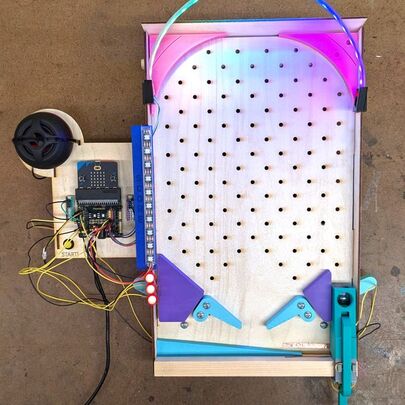 Custom-built electronic pinball machine with LED lights, flippers, control board, and wiring on a wooden frame.