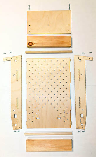 Flat lay of wooden pinball base parts and screws arranged on white background.