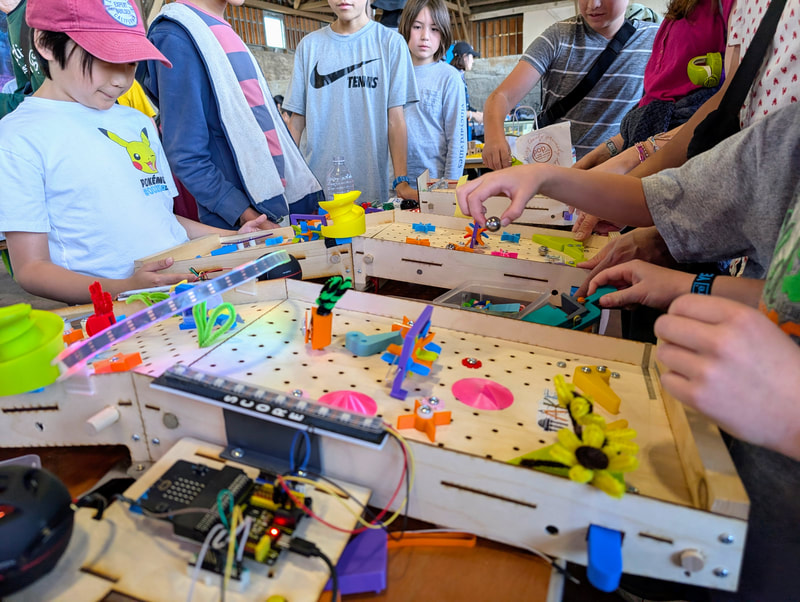 Children gathered around a custom wooden pinball machine with colorful parts and electronic wiring, actively playing and interacting.