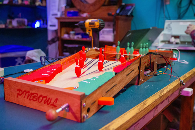 Close-up of a wooden tabletop bowling game with red and green pins set up on a blue table.