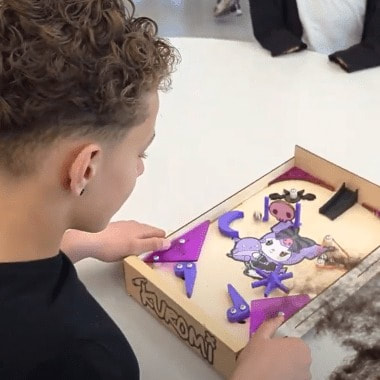 A young person playing a tabletop pinball game with a colorful design and purple flippers.