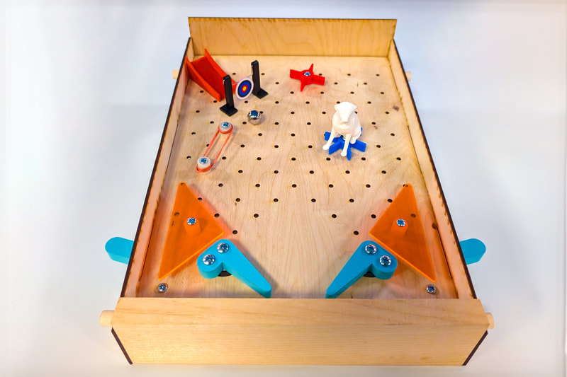 Wooden single-player DIY pinball machine with blue flippers, orange bumpers, a white dog figurine, and a target on a pegboard playing surface.