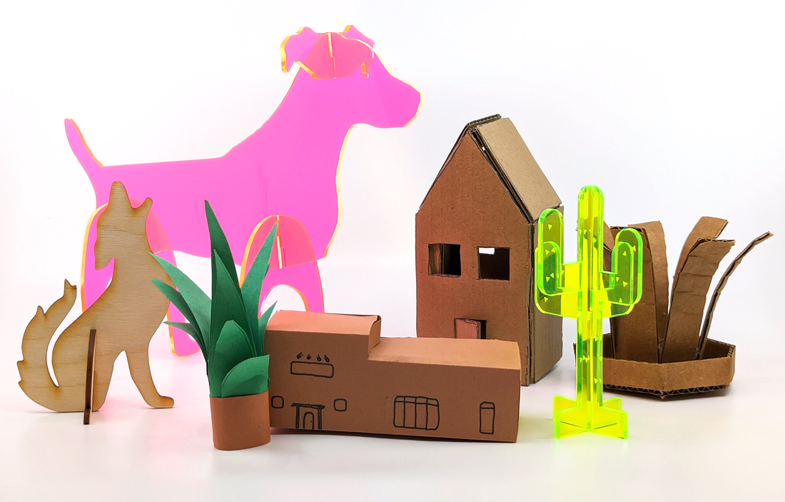Craft models including a pink translucent dog, a wooden cat, a green paper plant, two cardboard houses, and a yellow translucent cactus on a white background.
