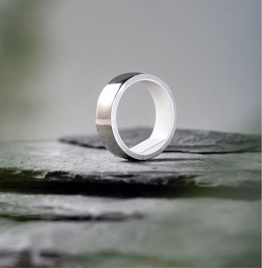 Shiny silver wedding band ring standing upright on textured gray stone surface.