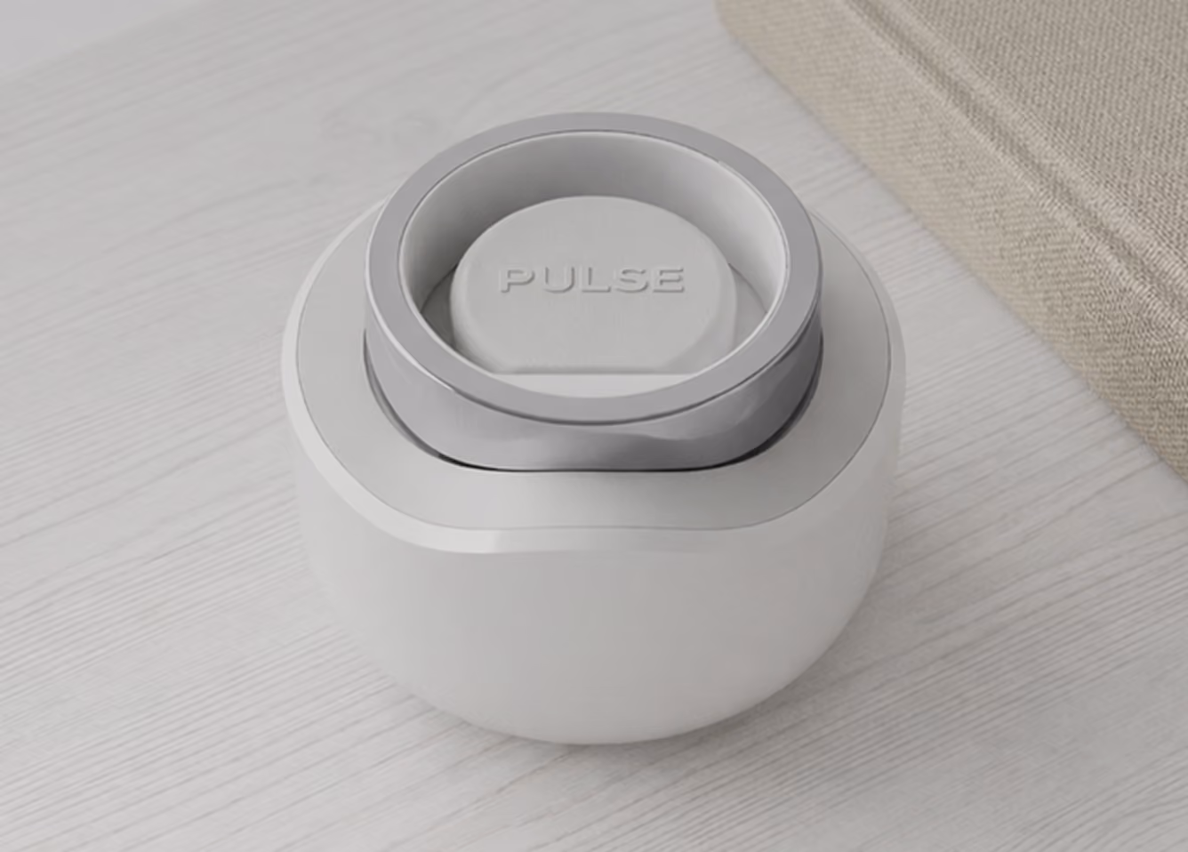 Small round white device labeled Pulse on a light wood surface near a beige fabric item.