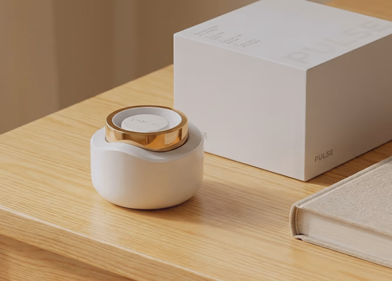 White and gold Pulse device on a wooden table next to its white box and a beige book.