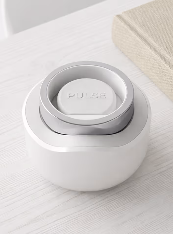 White and silver circular device labeled PULSE on a light wood surface next to a textured book.