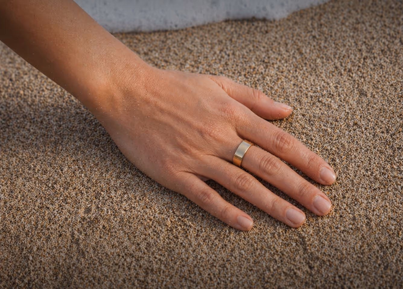Hand with gold ring resting on grain-covered surface with scattered grains on skin.