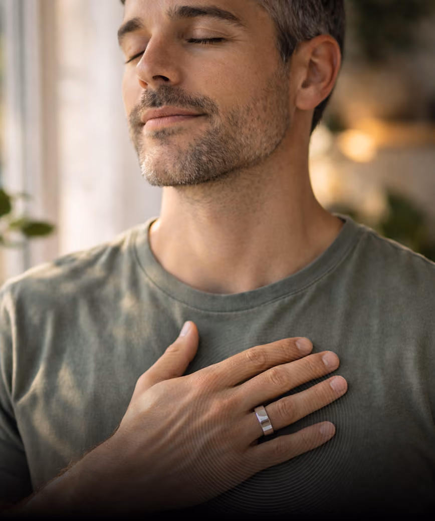 Man with closed eyes and hand on chest wearing a silver ring and green shirt in soft lighting.