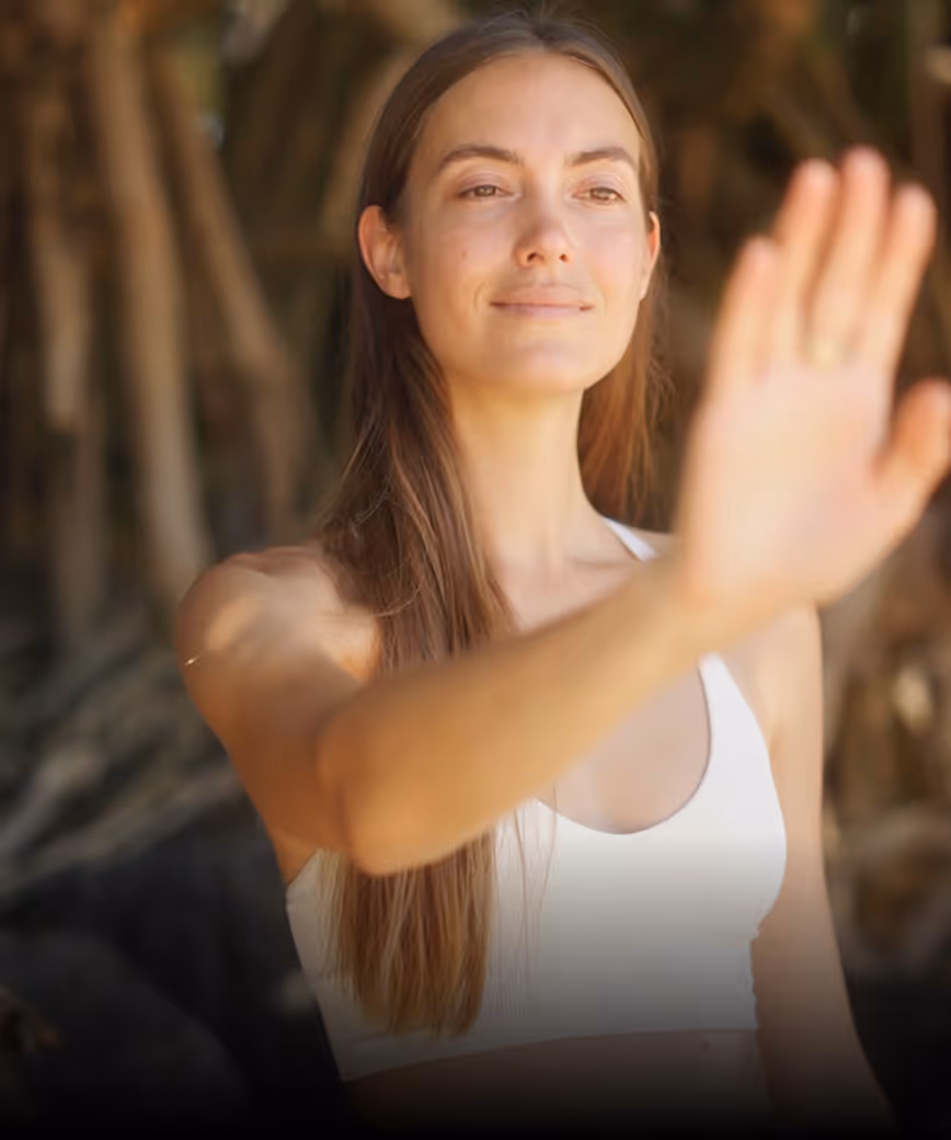 Woman in white top with long brown hair raising a hand in front with a calm expression.