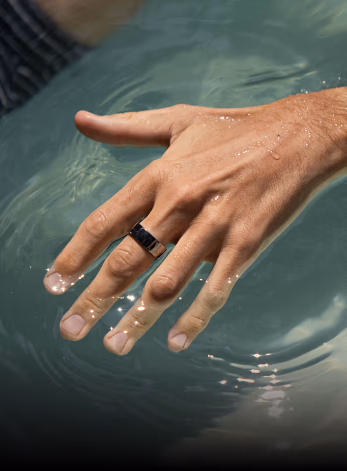 Male hand with a black ring partially submerged and wet in clear water, with light reflections.