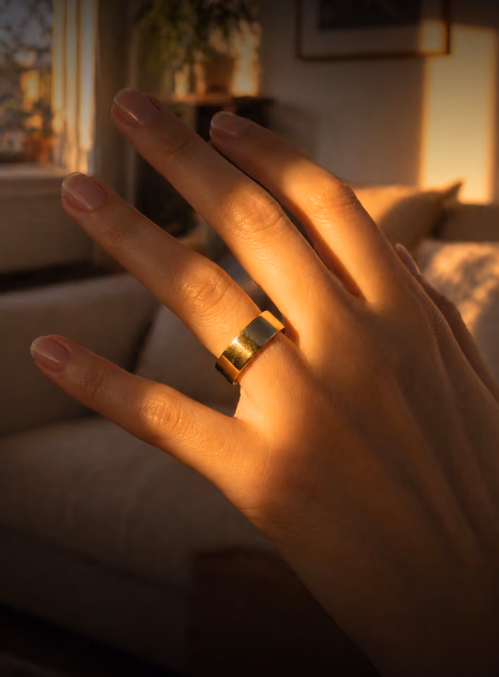 Hand with a smooth gold band ring on the ring finger lit by warm natural light indoors.