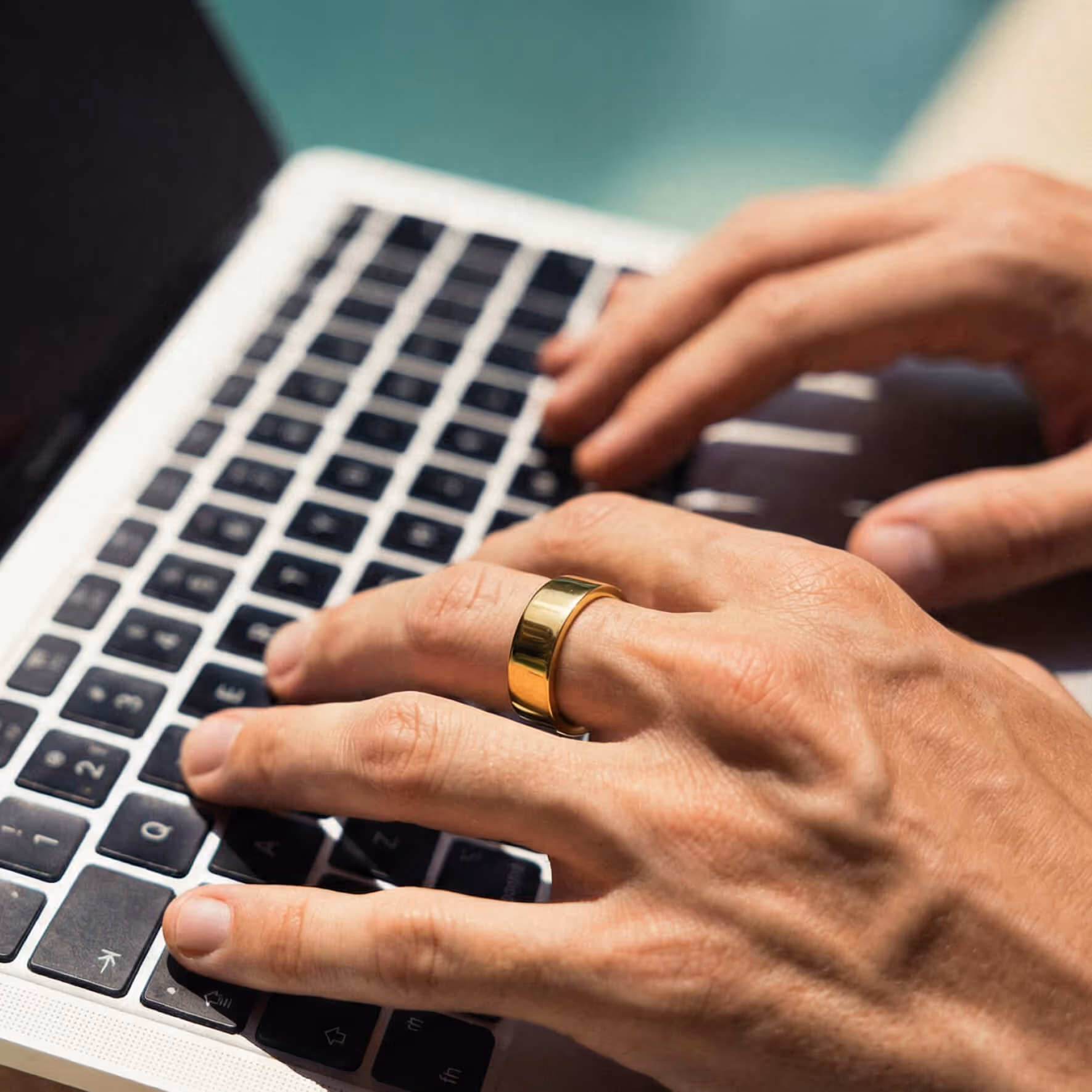 Close-up of hands typing on a laptop keyboard, wearing a shiny gold ring on one finger.
