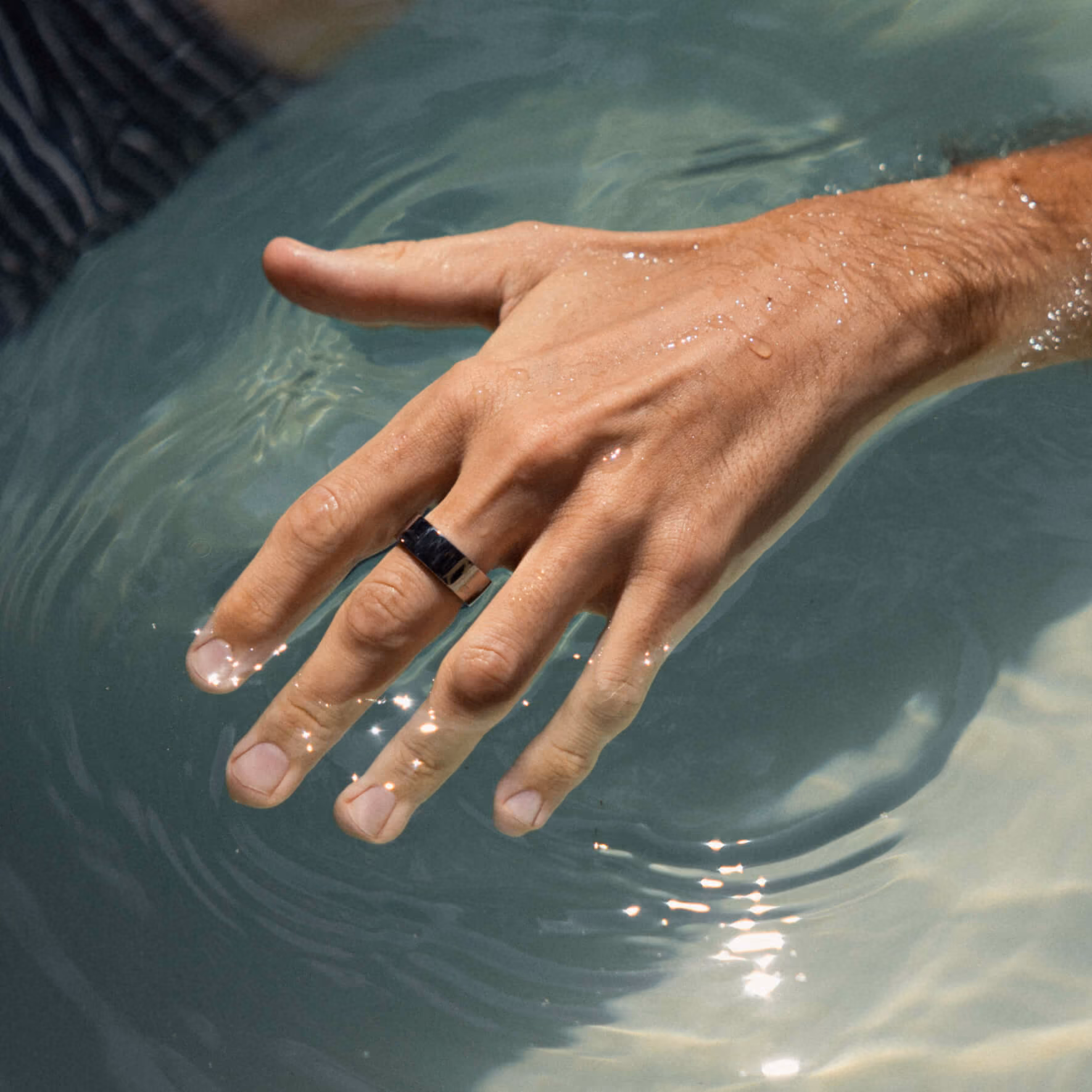 Hand with silver ring partially submerged in clear water with light reflections.