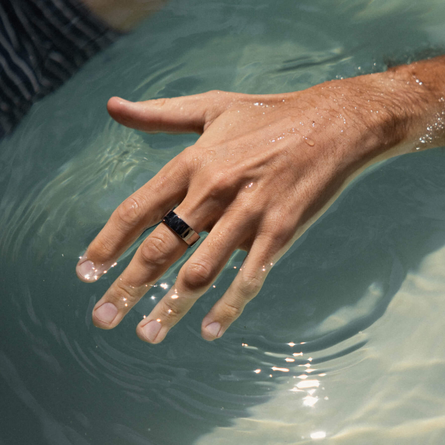 Hand with silver ring partially submerged in clear water with light reflections.