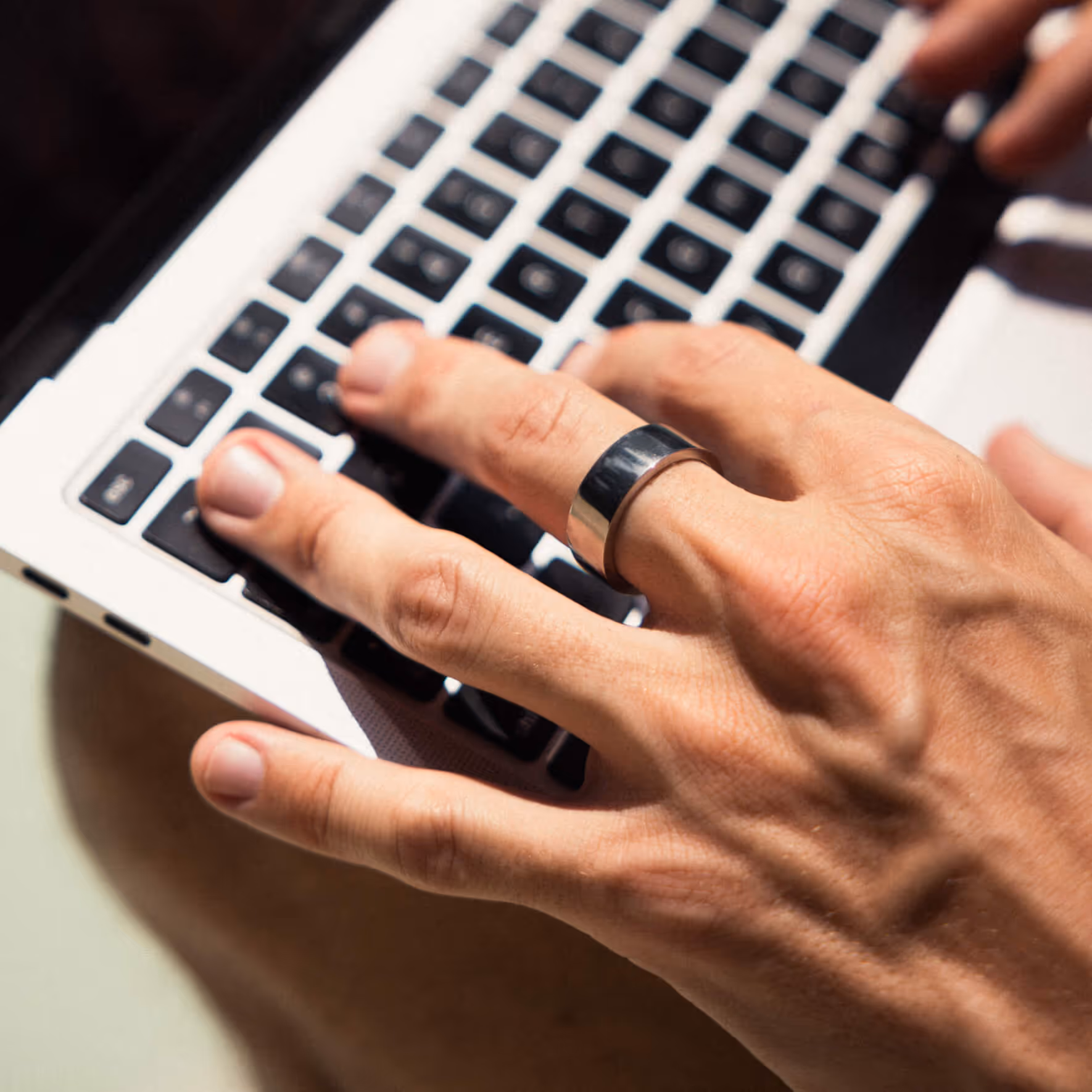 Close-up of a hand wearing a silver ring typing on a laptop keyboard.