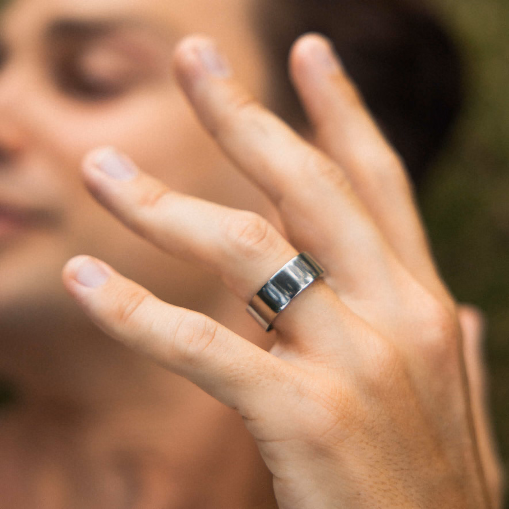 Close-up of a hand wearing a wide silver ring on the middle finger against a blurred background.