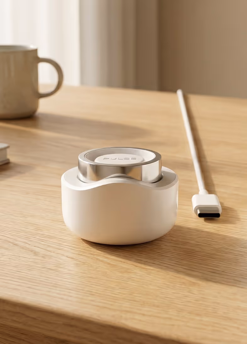 White and silver Pulse charging device on wooden table with a white USB-C cable and a mug in background.