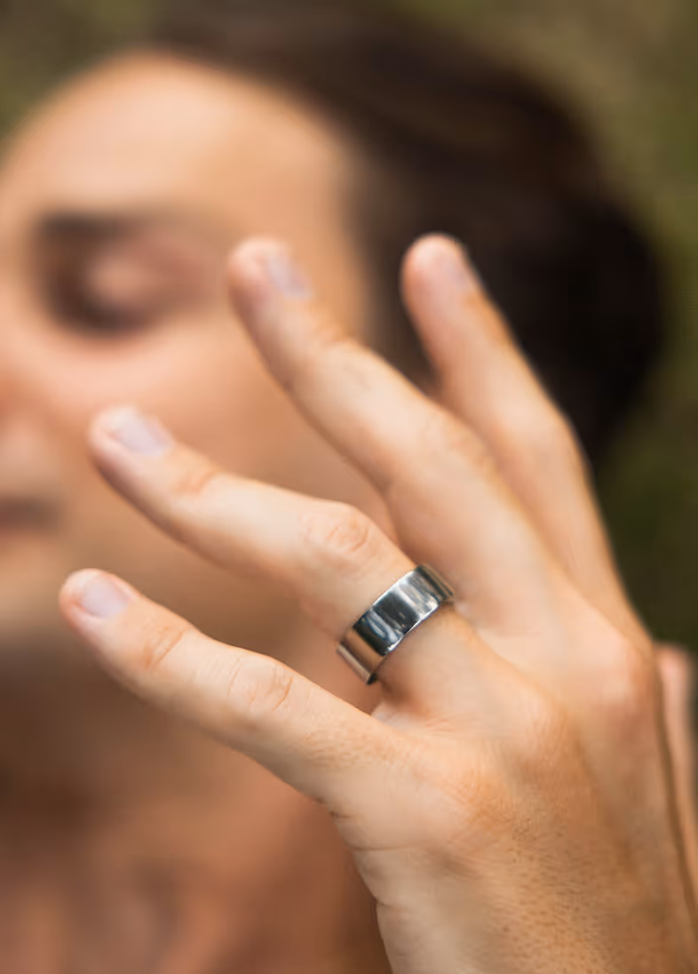 Close-up of a hand wearing a wide silver ring on the middle finger against a blurred background.