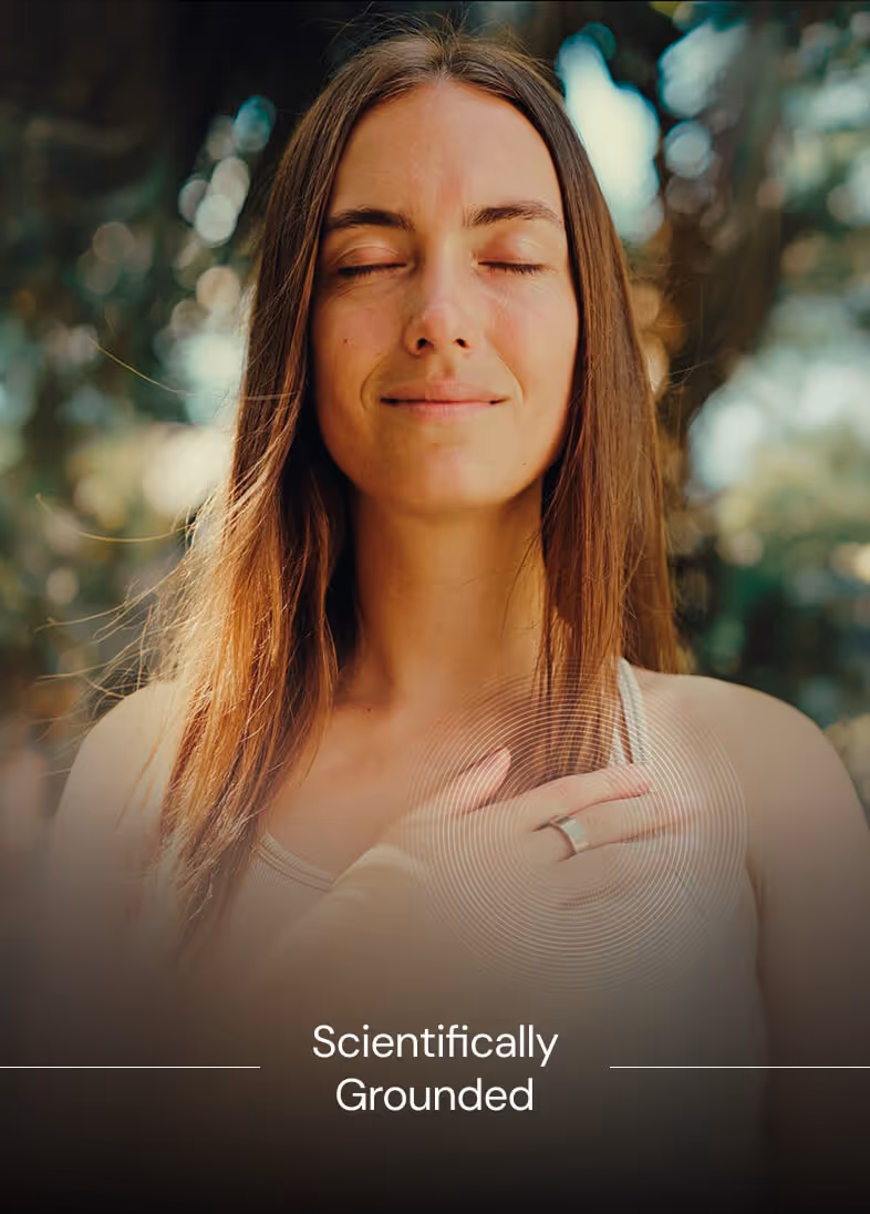 Woman with long hair eyes closed hand on chest wearing a silver ring and white tank top outdoors.
