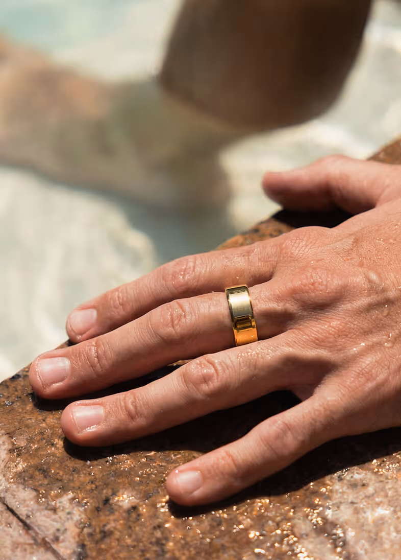 Close-up of a wet hand resting on a stone surface, wearing a plain gold ring on the ring finger.