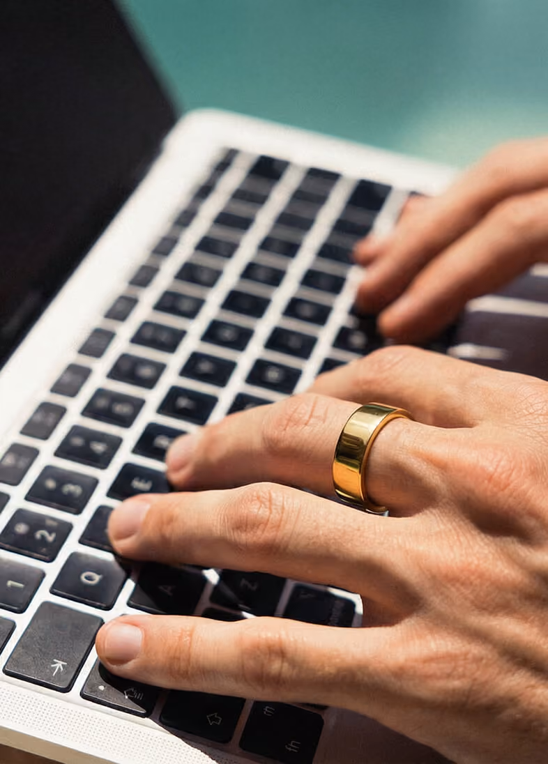Close-up of hands typing on a laptop keyboard with a gold ring on one finger.