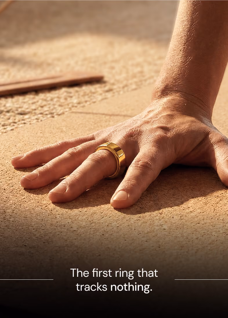 Close-up of a hand with a wide gold ring on the middle finger resting on a textured surface.
