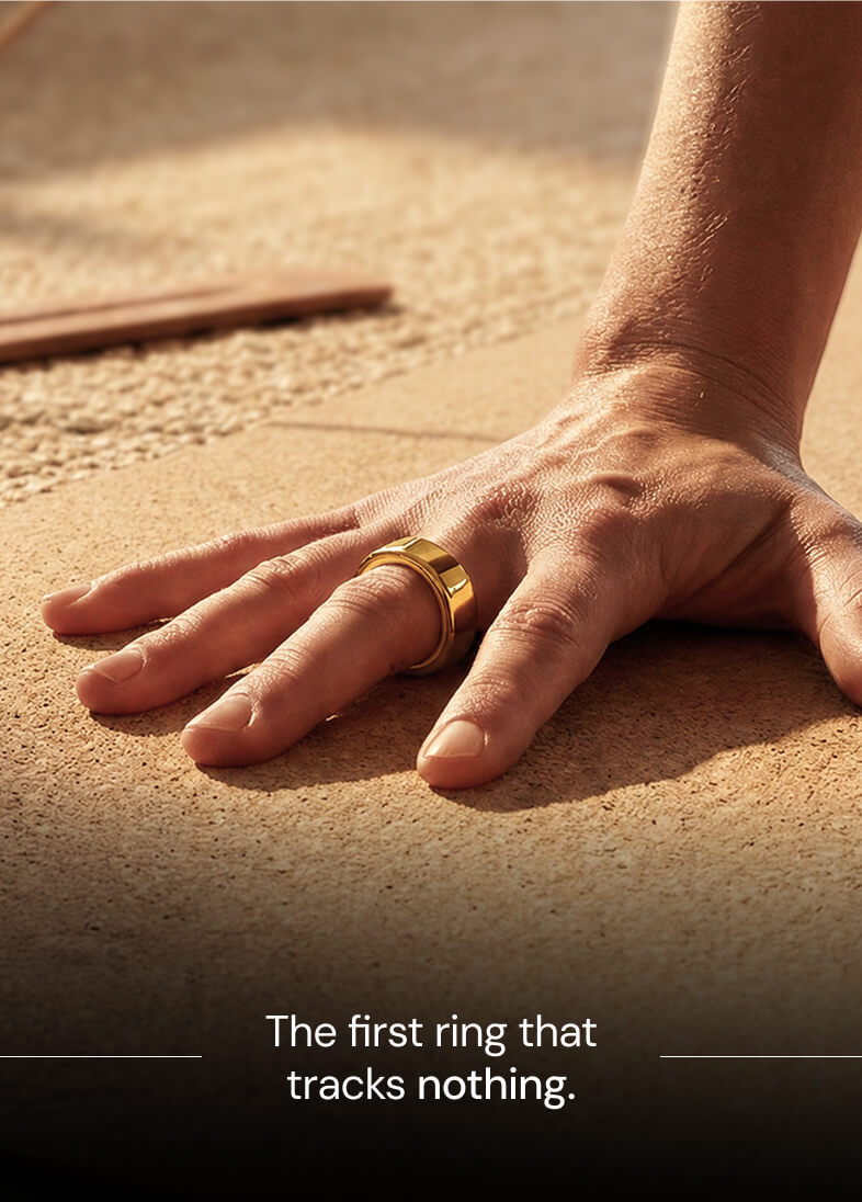 Close-up of a hand with a wide gold ring on the middle finger resting on a textured surface.
