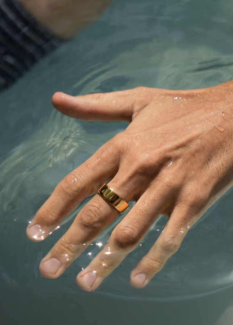 Close-up of a hand with a gold ring partially submerged in clear water.