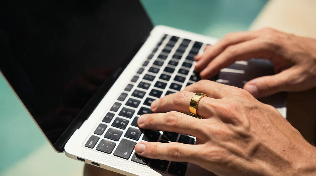 Hands typing on a laptop, one finger wearing the Pulse Ring
