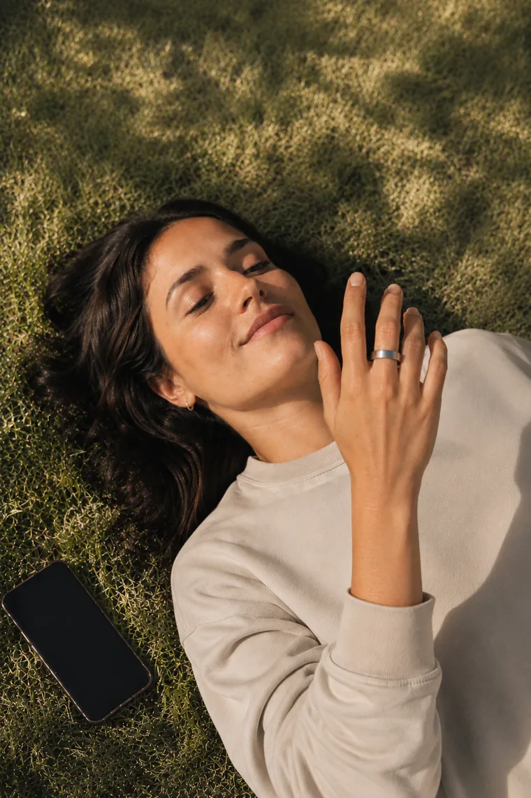 A woman resting on the grass with her eyes closed, wearing the Pulse Ring