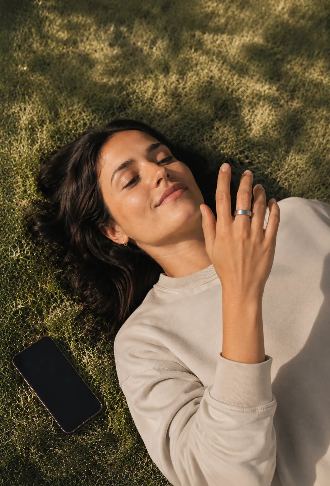 A woman lying on grass with her hand raised, wearing the Pulse Ring.