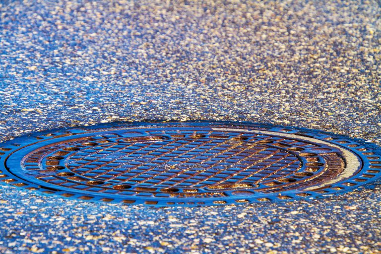 Close-up of a circular metal manhole cover on a textured asphalt surface.